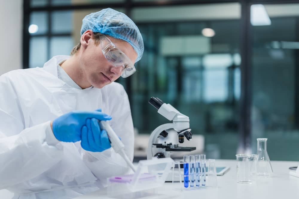Laboratory technician in protective gear working at a microscope during the Gram staining procedure